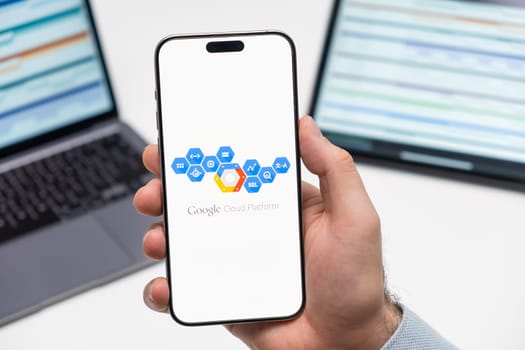 PRAGUE, CZECHIA - JULY, 2024: Google Cloud Platform logo on the screen of smartphone in mans hand and laptop on the background