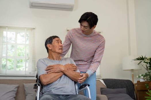 A son embraces his elderly father in a wheelchair, providing comfort and emotional support in a nurturing home environment.