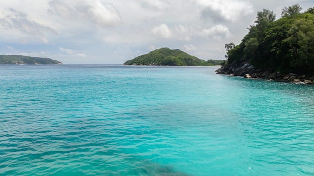 Turquoise waters embrace lush green islands under overcast sky. Seychelles, Mahe.