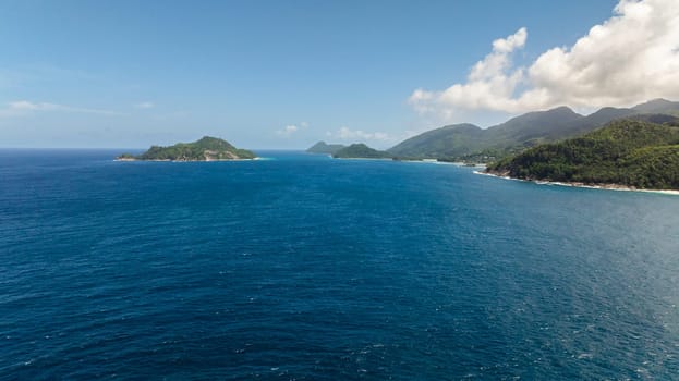 Granite boulders and ocean surf, set against a backdrop of verdant tropical forest. Seychelles, Mahe.
