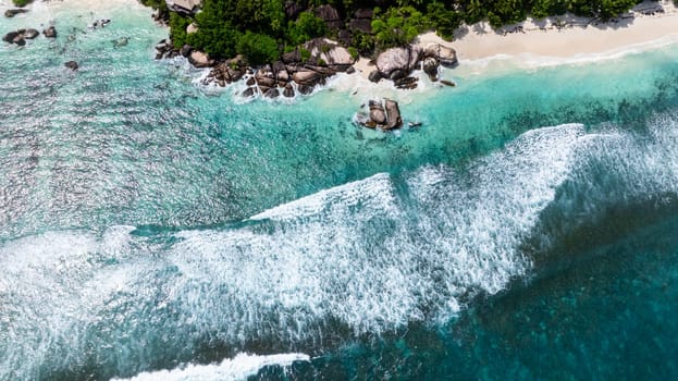 Turquoise waves crash against rocks along a scenic coast lined with lush vegetation. Seychelles, Mahe.