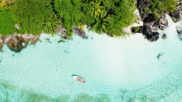 A single boat anchored by a small island surrounded by crystal clear waters and lush vegetation. Seychelles, Mahe.