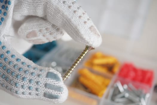A person in protective gloves holds a metal screw with various tools arranged.