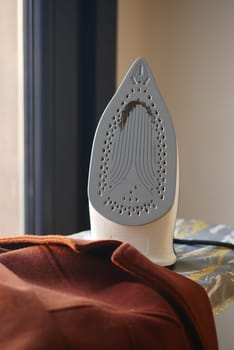 An iron is placed on clothing while sunlight brightens the room.