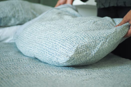 A person tidies up a pillow on a blue-patterned bedspread in a room.