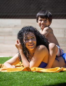 Mother and son are lying on a towel in the backyard, enjoying a sunny summer day