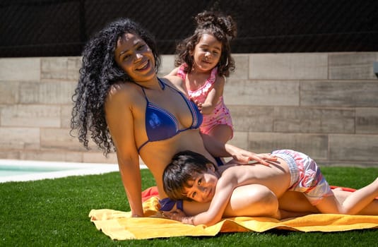 Happy mother in blue bikini relaxing by the pool with her two children on a sunny day