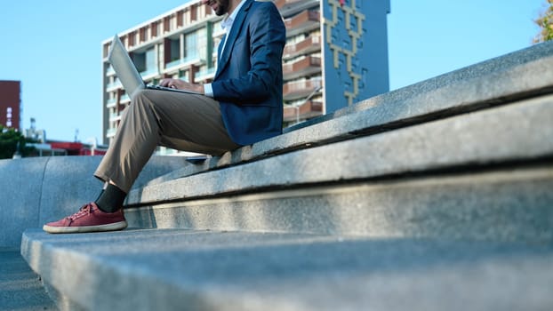 Cropped shot of businessman in suit sitting on steps in a city with a laptop.