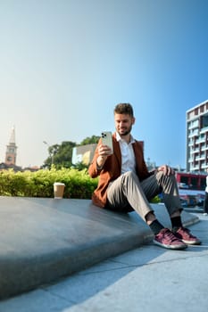 Smiling caucasian businessman using smartphone in front of a modern city backdrop.