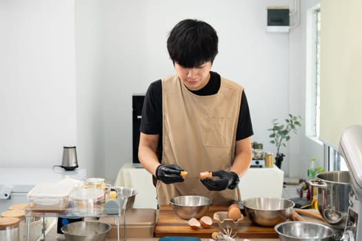 Male baker cracking an egg into mixing bowl preparing ingredients for homemade cookies.