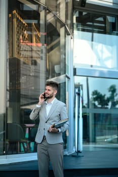 Business executive having a phone conversation outside a glass office building.