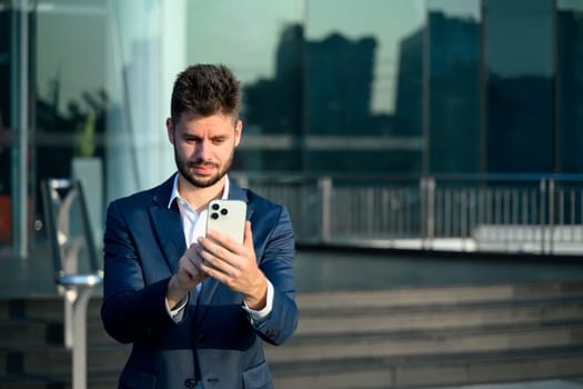 Professional businessman in a suit checking smartphone outside a contemporary office building.