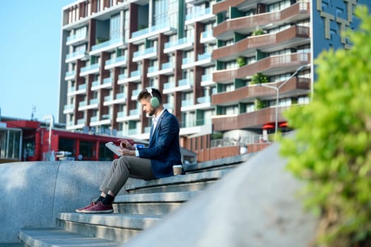 Young businessman with headphones working on digital tablet outdoors in the modern city.