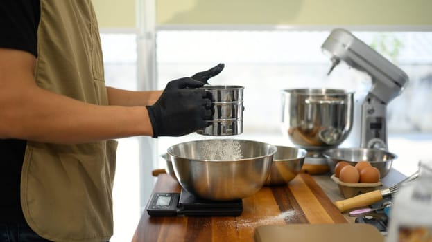 Baker sifting flour while preparing ingredients for cookie dough.