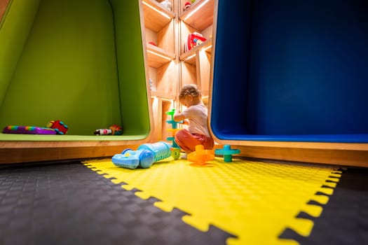 Toddler playing with toys in a colorful playroom with creative shelves and soft flooring