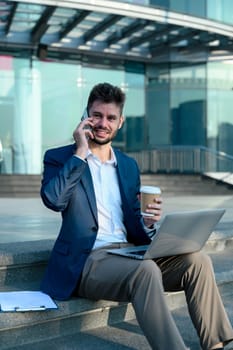 Businessman having a phone conversation while sitting on the steps of a modern building.