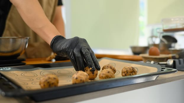 Close up of man placing chocolate chip cookie dough balls on baking tray.