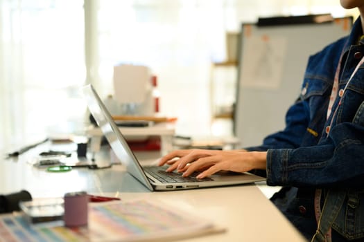Close up of designer hands typing on laptop in a creative workspace.