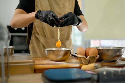 Male baker cracking an egg into mixing bowl preparing ingredients for homemade cookies.