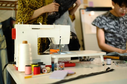 Close up of a modern sewing machine with thread and tools in a designer workspace.