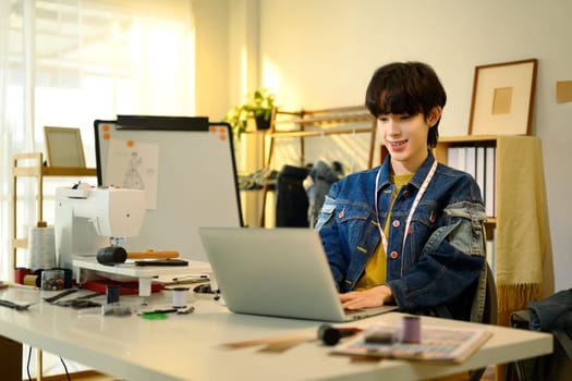 Fashion designer working on laptop in a creative studio.