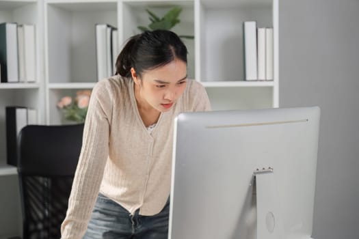 A woman leaning forward, focused on her computer screen while working in an office, showcasing dedication amidst potential office syndrome issues.