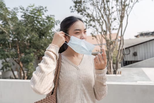 A young woman is smiling as she removes her protective mask while enjoying the outdoors in a public area, indicating a moment of freedom and joy.
