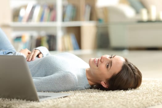 Happy woman with laptop lying on the floor in the living room at home