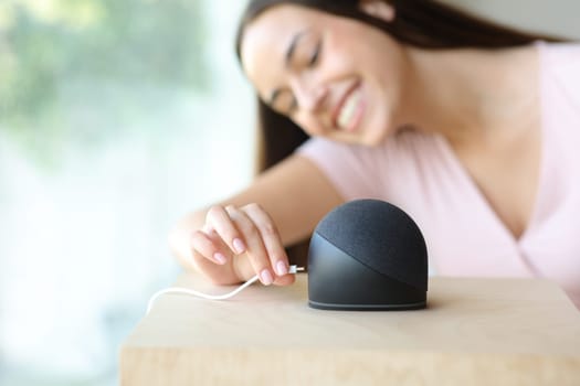 Happy woman plugging charger to her smart speaker at home