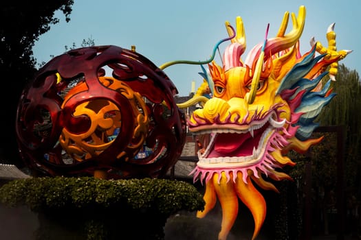 Vibrant orange and yellow Chinese dragon and ball sculpture, with water mist. Located in Beijing near Beihai Park
