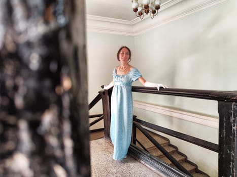 The girl dressed as a romantic princess presents a graceful pose in the ancient castles staircase, embodying a vintage aesthetic.