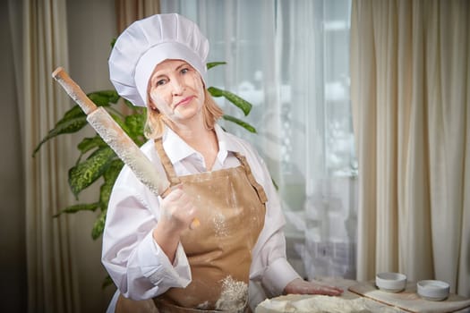 An elderly woman joyfully prepares dough with flour in a cozy kitchen, capturing a fun moment during her playful baking session.