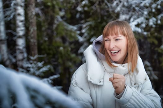 A middle-aged woman joyfully walks through a snowy forest, celebrating the festive atmosphere of winter and the upcoming New Year.