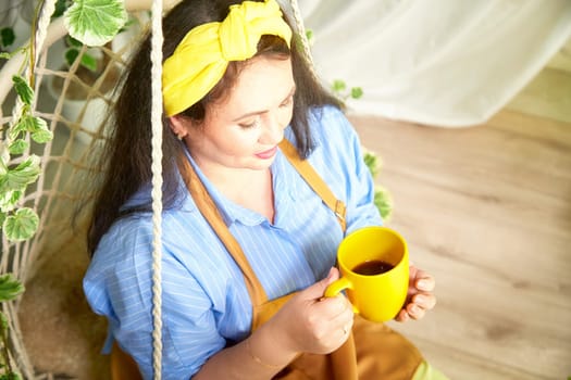 A gardener relaxes with a cup of tea in a vibrant greenhouse filled with plants.