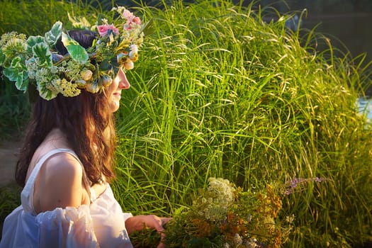 Slavic plump chubby girl in long white dress on the feast of Ivan Kupala with flowers and water in a river or lake on summer evening
