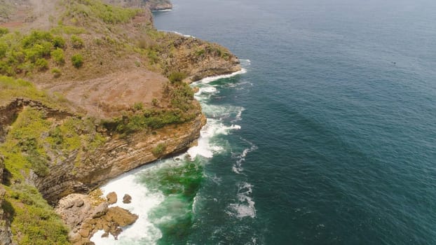 aerial view rocky coastline with cliffs, ocean surf with breaking waves in coast. seascape waves break on rocky shore java, indonesia