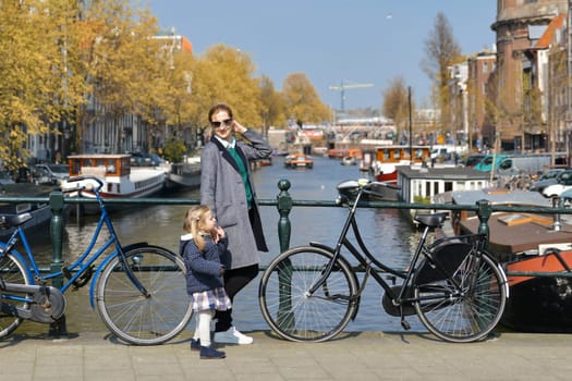 Blonde Dutchwoman mother with her daughter near the bicycle on the bridge over the water channel in Amsterdam city in autumn