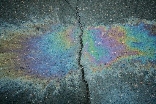 Colorful oil spill creating patterns on cracked pavement surface