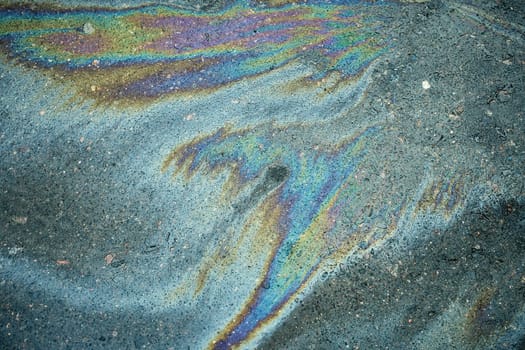 Rainbow-hued gasoline leak forming a colorful sheen on the dark surface of the asphalt road