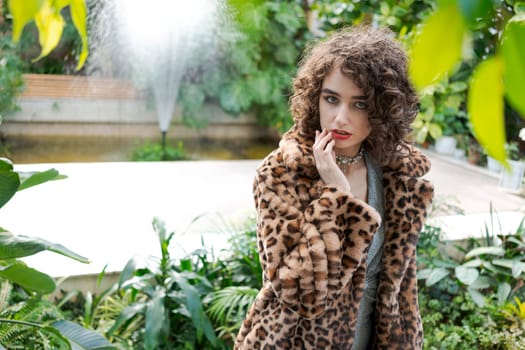 Woman wearing a leopard print coat poses in front of a fountain. She is wearing a necklace and has red lipstick on