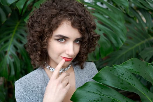 Woman with curly hair is posing for a picture. She is wearing a necklace and a red shirt
