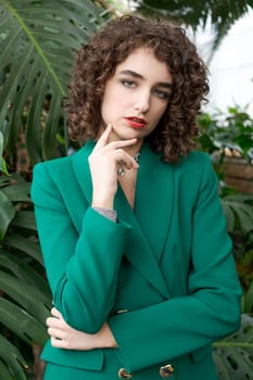 Woman in a green jacket is posing for a photo. She is wearing a watch and a necklace