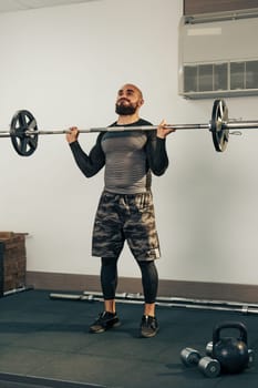 A man is engaged in a weight lifting routine, executing an overhead barbell lift with proper form. He wears athletic gear and is focused on building strength in a well-equipped gym.