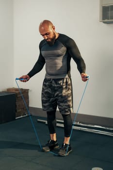 A man wearing a fitted black top and camo shorts skips rope in a gym environment. Fitness equipment is visible nearby, indicating an active workout session.