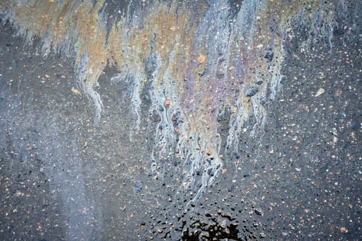 Motor oil or fuel spill creating a stain on wet asphalt of parking lot