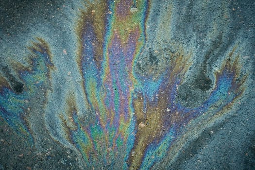 A spill of gasoline forms striking patterns on the asphalt, indicating environmental contamination and a hazardous driving condition