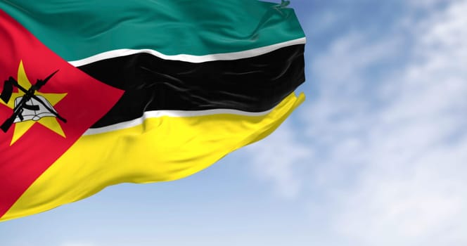 Close-up of Mozambique national flag waving on a clear day. Green, black, and yellow stripes, red triangle, yellow star, crossed book, hoe, and AK-47. 3d illustration render. Selective focus. Close-up