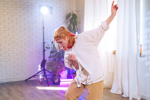 A young woman energetically dances in a modern studio filled with natural light. The space is decorated with plants and a soft color palette that enhances the artistic atmosphere.