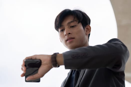 A businessman in a suit checking the time on his smartphone outdoors, demonstrating punctuality and professionalism.