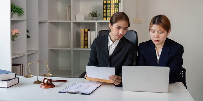 A lawyer and client working together on legal documents while reviewing information on a laptop in a contemporary office space.